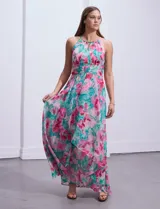 Vestido largo de gasa estampada con flores rosas y turquesas sobre fondo blanco. Tiene escote halter con ojal, cintura fruncida y falda con sobrecapa.