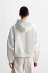 Sudadera color crudo, estilo hoodie, corte boxy, con capucha, manga larga, bolsillo tipo canguro y terminaciones en rib.