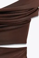 Vestido largo marrón de tejido fluido con escote asimétrico de un solo hombro, detalle de frunces y abertura cut out en la cintura.