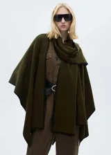 Poncho verde militar de tejido de punto grueso con ribetes negros en contraste y cuello alto.