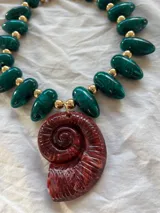 Collar maximalista con mostacillas verdes y dije de caracola rojo.