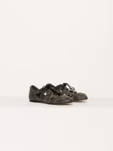 Zapato bajo acordonado de cuero texturado color negro, con diseño calado y aplique metálico con el logo de la marca.