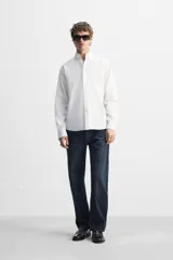 Camisa blanca de corte regular fit confeccionada en popelín de algodón. Tiene cuello abotonado, manga larga con puños abotonados y cierre frontal con botones.