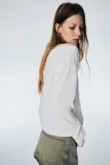 Buzo de punto fino color blanco, con escote amplio tipo barco que deja los hombros descubiertos, manga larga y puños y bajo acanalados.