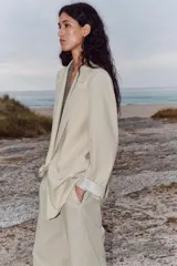 Blazer negro de lino con cuello solapa y escote pico. Manga larga con hombreras y puños con vuelta estampada a rayas. Bolsillos con solapa en el delantero, forro interior y cierre frontal con botón.