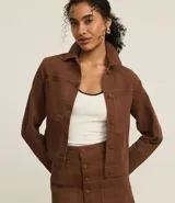 Campera marrón de sarga con textura cotelê, corte regular, cuello inglés, manga larga, abotonada y con bolsillos delanteros.