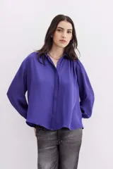 Camisa blanca de manga larga confeccionada en viscosa con acabado sandwash, de textura suave y aterciopelada. Cuello camisero con botón en forma de corazón y frunces en el canesú delantero y la espalda.