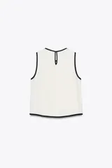 Blusa blanca sin mangas de crepe con cuello redondo y detalle de ribete negro en cuello, sisas y abertura frontal diagonal.