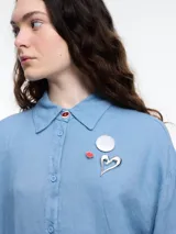 Camisa celeste de calce relajado con abertura en la espalda y mangas largas. Confeccionada en tejido liviano de lino y viscosa. Incluye tres pins decorativos.