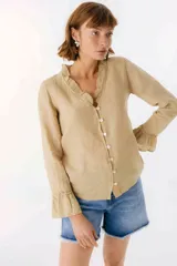Blusa blanca de lino con botones de nácar, volados en el escote y mangas largas con puños acampanados. Corte recto y holgado.