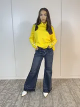 Sweater amarillo de cuello alto, corte holgado y mangas largas con botones decorativos en los puños.