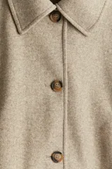 Campera corta color beige de tejido de fieltro suave con cuello clásico y cierre frontal con botones. Modelo de corte holgado con hombros caídos, bolsillos insertados y sin forro.