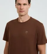 Remera marrón de algodón, corte comfort, con cuello redondo y mangas cortas. Presenta un pequeño estampado de palmera en el pecho.