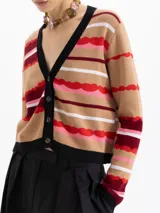 Cardigan corto de punto con estampado de rayas onduladas en tonos beige, rojo, rosa y blanco. Tiene cuello en V, botones frontales y ribetes negros en el escote y puños.