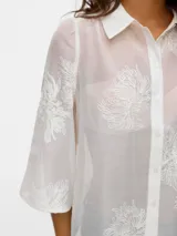 Camisa blanca traslúcida con bordado de flores blancas, de manga 3/4 con cuello camisero y calce regular. Con mangas amplias, puños anchos y cierre de botones.