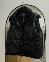 Chaleco negro de ecocuero con cuello alto, cierre frontal con broches a presión, bolsillos laterales y diseño acolchado.