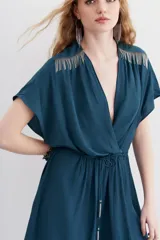 Minivestido negro de escote cruzado, mangas cortas y cintura elastizada con lazo. Presenta cadenitas metálicas en los hombros y en los extremos del lazo.