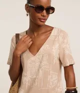 Vestido corto tipo t-shirt color beige con estampado de follaje y arquitectura, escote en V y mangas cortas.