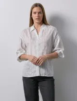Camisa texturada blanca con líneas verticales negras, marca Hester & Orchard. Cuello a la base, escote en V y abertura central con botones. Manga ¾ con terminación fruncida.