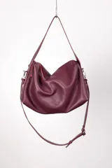 Bolso tipo hobo de cuero color borgoña con interior rojo, cierre superior con cremallera y doble correa: una corta para llevar al hombro y otra larga regulable para usar cruzada.
