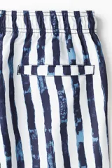 Short de baño blanco con rayas verticales azules, cintura elástica con cordón ajustable, bolsillos laterales y bolsillo trasero con cierre autoadherente. Cuenta con suspensor interior de malla suave.