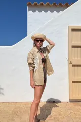 Camisa beige de lino con bordado de concha marina en el frente, de corte recto y mangas largas.