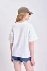 Remera blanca de corte cuadrado con estampa fotográfica de palmeras y edificio.