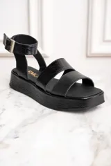 Sandalias negras de cuero con plataforma y dos tiras sobre el empeine, una de cuero liso y otra charolada. La tira del tobillo es de cuero con textura tipo cocodrilo y hebilla metálica.
