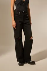 Pantalón jean negro con roturas en las rodillas, diseño de estrellas metálicas a lo largo de las costuras laterales y en los bolsillos delanteros.