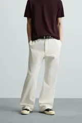 Pantalón negro de algodón con corte relajado y pierna ancha (flare fit). Presenta cierre frontal con botón y cremallera, bolsillos delanteros y bolsillos traseros de plastrón.