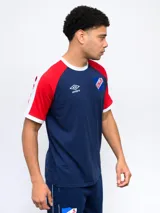 Remera de algodón azul con mangas ranglan azul marino y detalles en blanco en cuello y puños. Incluye logo de Umbro y escudo del Club Nacional de Football en el frente.