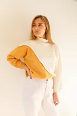 Sweater de punto color crema y mostaza, con cuello cisne y diseño asimétrico.