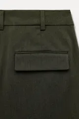 Bermuda larga color verde oscuro de tiro medio y pierna ancha. Confeccionada en hilatura con 19% de lana. Presenta trabillas en la cintura, bolsillos laterales y con solapa en la espalda, pinzas en el delantero y cierre frontal con cremallera y botones.