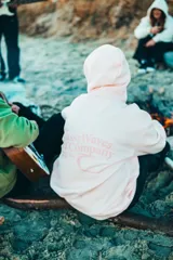 Buzo hoodie rosa con capucha y cordones ajustables. Estampado en la espalda con el texto "ClassyWaves Surf Company" y un logo de una ola.