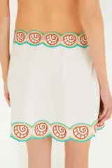 Minifalda playera blanca con bordados de palmeras, olas y conchas en tonos naranja, verde, celeste y amarillo. Tiene lazos laterales para ajustar a la cintura.