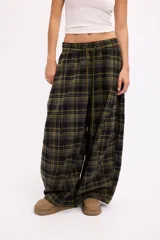 Pantalon de corte oversize y tiro medio, confeccionado en tela con estampado de cuadros en tonos marrones y negros. Presenta una silueta amplia y holgada con cintura elástica y cordón ajustable.