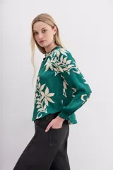 Camisa holgada verde esmeralda con estampado floral en color crema, escote redondo con abertura frontal y lazo de ajuste, mangas largas con puños elastizados con volados.