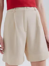 Short de sastre color beige claro, de tiro alto, con pinzas frontales y dobladillo ancho en el ruedo.