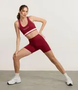 Bermuda deportiva femenina color bordó, tiro alto, confeccionada en microfibra. Presenta un recorte lateral contrastante de color rosado claro que recorre la pierna.