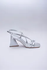 Sandalias de tacón alto color violeta metalizado, con tiras finas cruzadas en el empeine, puntera cuadrada y cierre con hebilla en el tobillo. El tacón es geométrico con forma de triángulo invertido.