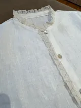 Camisa blanca de lino con cuello mao y detalle de puntilla de algodón en cuello y cartera de botones. Cierre frontal con botones de nácar.