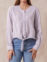 Blusa de algodón a rayas verticales finas en tonos lila y blanco, marca Dash. Escote en V y abertura frontal con botones. Mangas largas regulables con presilla y botón. Terminación de ruedo anudado.