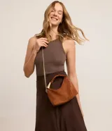 Bolso bandolera pequeño de gamuza color marrón con asa corta rígida y correa de cadena dorada.