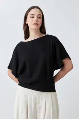 Blusa negra con textura amasada, de mangas cortas y corte holgado.