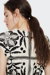 Vestido corto sin mangas de algodón color crudo con estampado de flores, hojas y lunares en negro. Tiene escote cruzado en V, cintura elastizada y falda con vuelo.