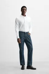Camisa blanca de algodón, corte regular, con cuello italiano abierto, manga larga con puños abotonados y cierre frontal con botones.