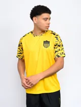 Remera de fútbol amarilla con mangas negras con diseño geométrico y escudo del Club Atlético Peñarol en el pecho.