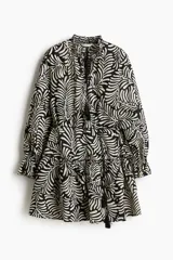 Vestido corto con cuello mao fruncido, escote en V con lazos y mangas largas abullonadas con puños elásticos. Tiene estampado de hojas en blanco y negro, corte a la cintura con cordón ajustable y falda escalonada con volantes.