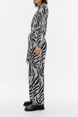 Mono largo estilo cargo con estampado animal print en blanco y negro. Tiene cuello con tira, manga larga con puño y botones de presión, suave fruncido en cintura y cinturón de tela con trabillas. Cierre frontal con botonadura de presión y bolsillos con pespuntes en el delantero.