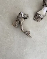 Sandalias de tacón alto con estampado de piel de serpiente, tira delgada sobre los dedos y pulsera al tobillo con hebilla metálica.